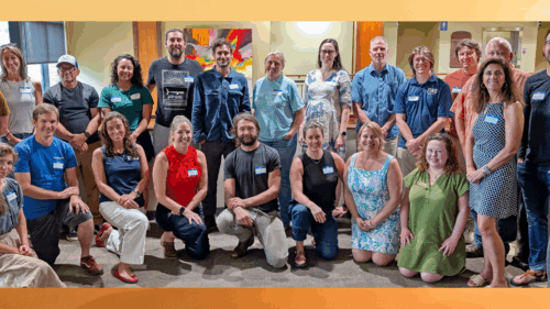 Group photo of the new members of the Waypoint Resilience Cohort standing and sitting together in a bright indoor space, smiling and wearing name tags.